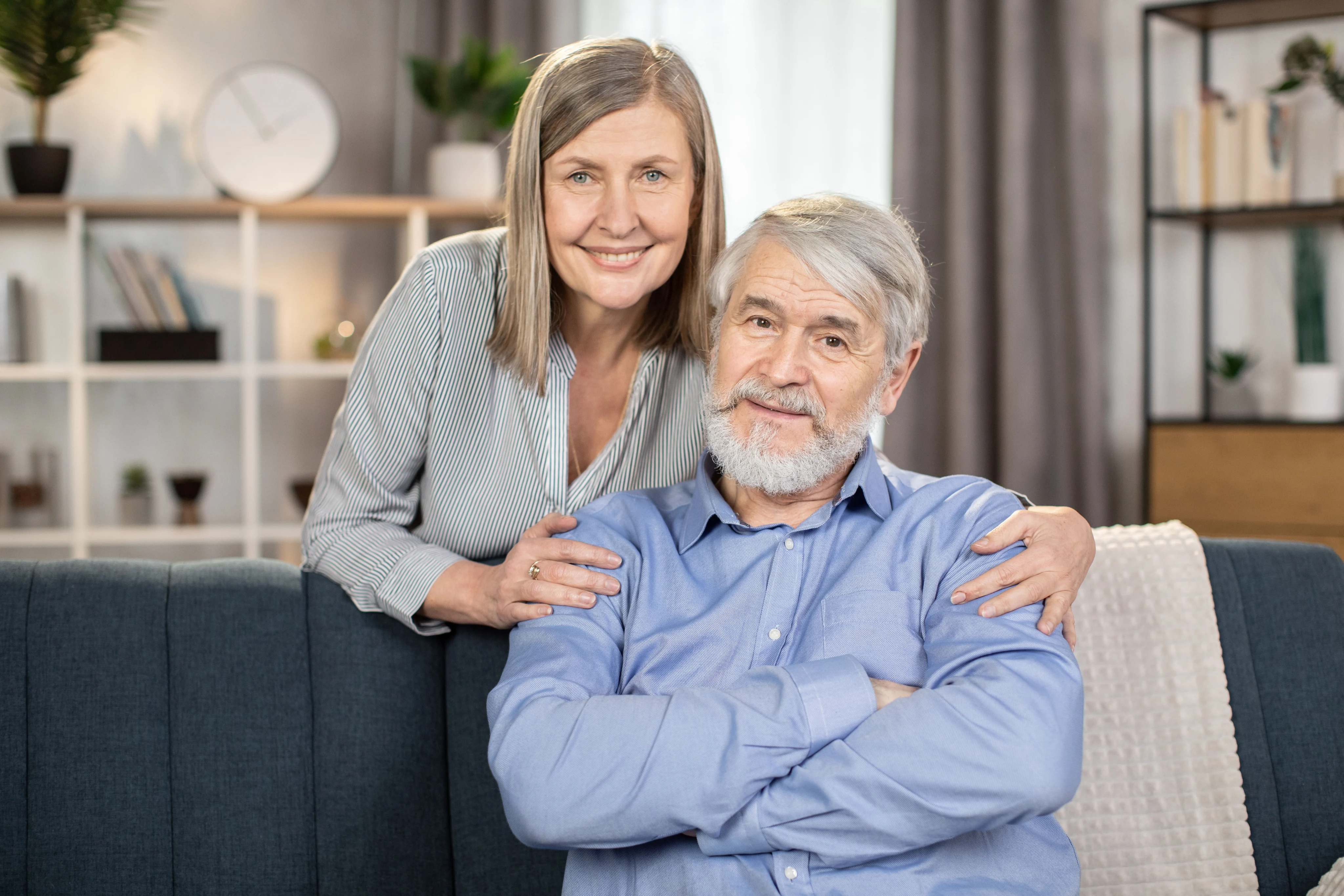 Uśmiechnięta para seniorów: kobieta obejmuje siedzącego mężczyznę